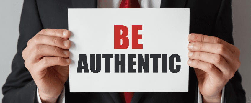 A person holds a "Be Authentic" sign with the capital words 'Be' highlighted in bold in red
